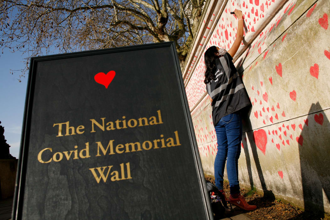 A woman draws red hearts representing individual coronavirus deaths onto the National Covid-19 Memorial Wall in London, England, on March 30, 2021.