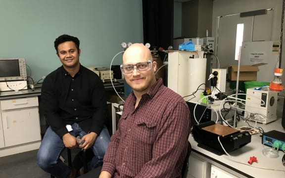 Taniela Lolohea and Daniel Carlton are sitting on stools in a physics lab in front of scientific equipment.