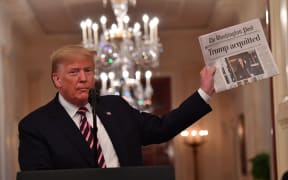 US President Donald Trump holds up a newspaper that displays a headline "Acquitted"  while speaking about his Senate impeachment trial in the East Room of the White House in Washington, DC, February 6, 2020.