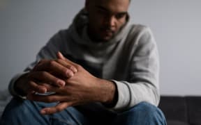 a man in a grey hooded sweatshirt wringing his hands together