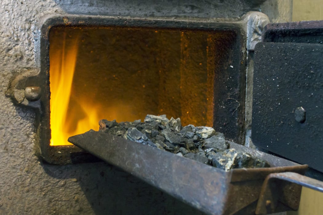 Hot water boiler with open door and fire inside and scoop with coal.