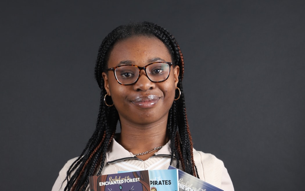 Rutendo Shadaya is smiling at the camera and holding her three books fanned out in front of her.