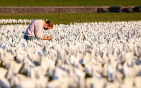 A person kneels to take photos of some of the more than 670,000 white flags covering 20 acres of the National Mall in an art memorial for Covid-19 victims by Suzanne Brennan Firstenberg In America: Remember.