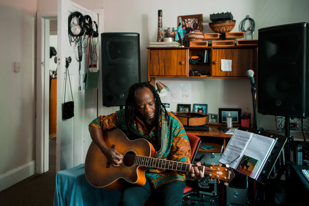 Judah Seomeng playing guitar in his house in Te Whanganui-a-Tara