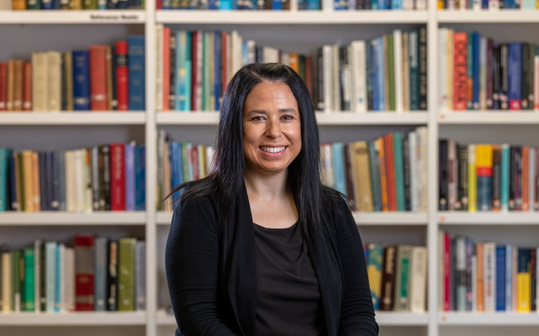 A woman stands in front of shelves of books. She is smiling at the camera.
