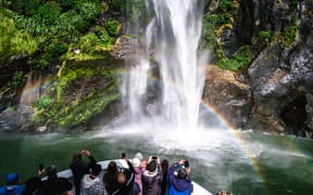 A group of tourists enjoying a stunning scene of nature while cruising into waterfall in Milford Sound, New Zealand.