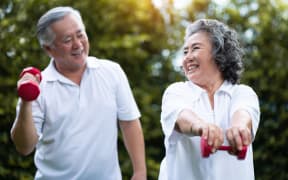 Asian Senior Couple exercising with red dumbbells at the outdoor park togetherness. Smiling Chinese or Thai or Japanese people.