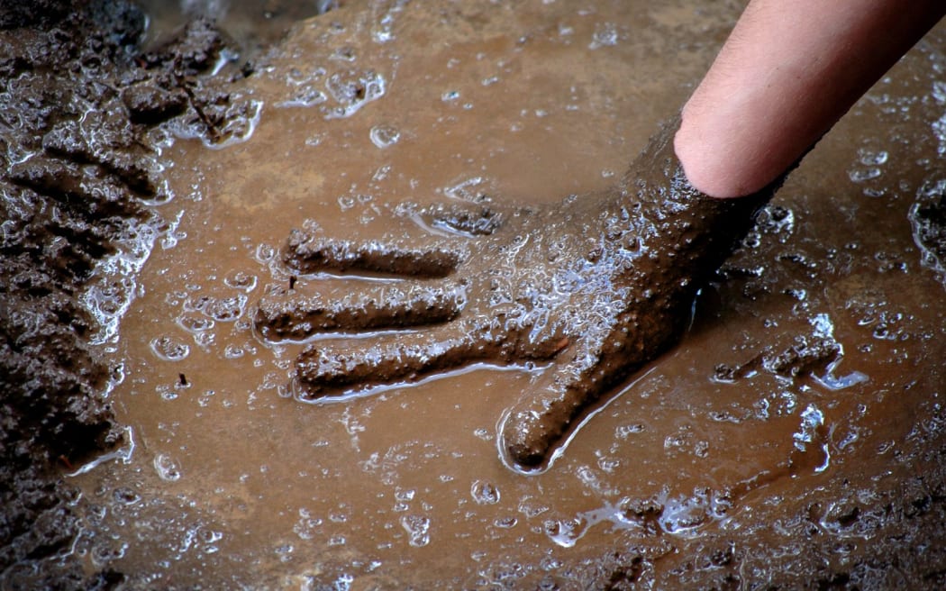 Child with hand in mud and water playing muddy games wet
