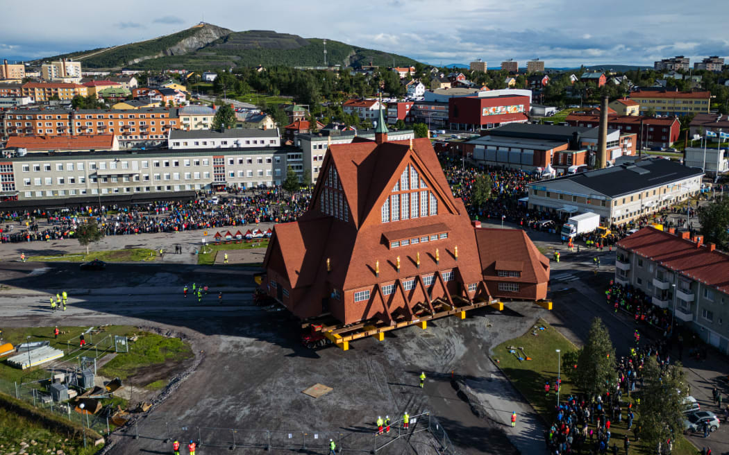 An aerial view shows people gathered to watch the moving of the wooden Kiruna Church, in Kiruna, Sweden on August 19, 2025. The church is being moved five kilometers to the new center of Kiruna due to the expansion of the iron ore mine operated by state-owned Swedish mining company LKAB. (Photo by Jonathan NACKSTRAND / AFP)