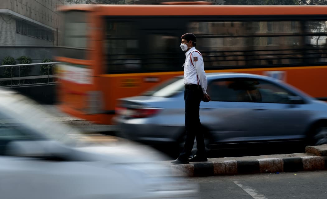 An Indian traffic policeman with his face covered by a protective mask handles traffic at an intersection in New Delhi