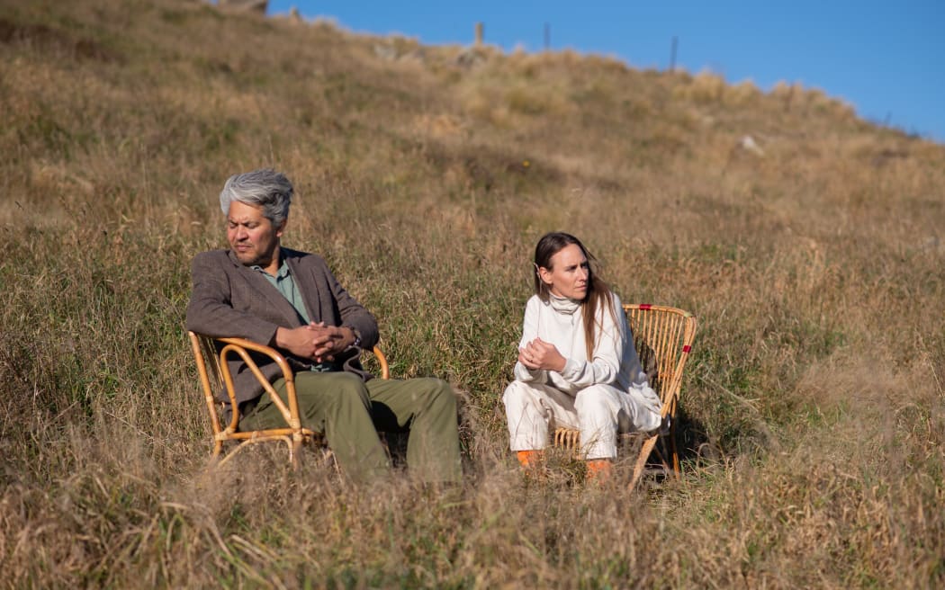 Musicians Lauren and Matt Barus sit on chairs in a paddock of grass staring away from the camera.