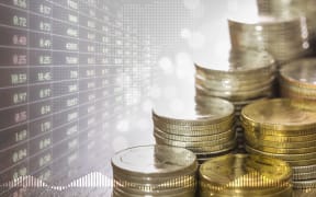 Stacks of coins money and faded stock trading board in golden light and soft bokeh with digital world map on background