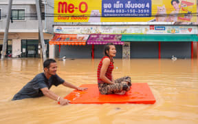 A man transports a woman through flood waters in Hat Yai in Thailand's southern Songkhla province on November 26, 2025, as severe flooding affected thousands of people in the country's south following days of heavy rain. Tens of thousands of people in Thailand and neighbouring Malaysia were displaced by widespread flooding, with streets submerged, homes inundated and at least 34 dead, officials said November 26. (Photo by Arnun Chonmahatrakool / THAI NEWS PIX / AFP)
