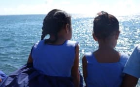 Young schoolgirls sit on the foreshore in Apia