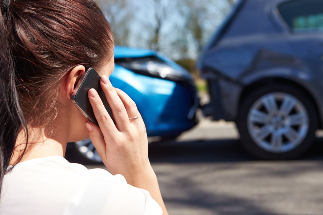 A woman makes a phone call, looking at a minor accident between two cars.