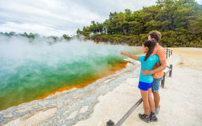 New Zealand travel tourists couple at Champagne pool at Wai-O-Tapu pools Sacred Waters. Tourist attraction in Waiotapu, Rotorua,