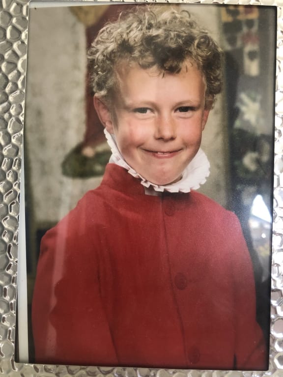 A framed picture of Emile as a young boy. He is wearing red velvet church robes and smiling at the camera.