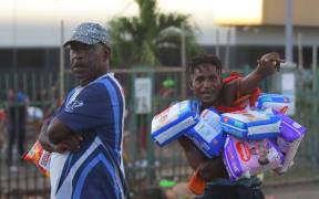 Two men carry looted goods amid a state of unrest in Port Moresby on January 10, 2024. Papua New Guinea's prime minister declared a 14-day state of emergency in the capital on January 11, 2024, after 15 people were killed in riots as crowds looted and burned shops. (Photo by STRINGER / AFP)