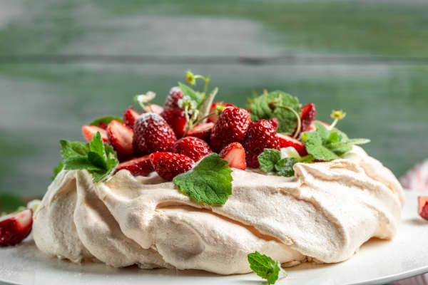 Homemade delicious meringue cake Pavlova with whipped cream, fresh strawberries and mint on wooden background, close up view.