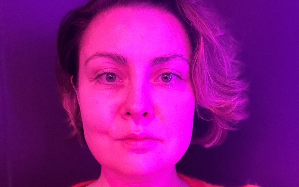 A woman is looking directly at the camera with illuminated by neon light