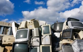 A pile of old computer screens  in a landfill, against a blue sky.