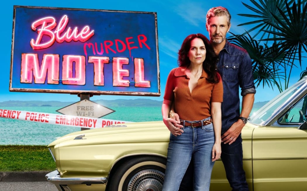 Stars Michala Banas and Brett Tucker stand in front of the Blue Murder Motel sign.