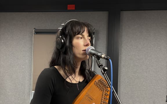 Georgia Knight is singing into a microphone and playing the autoharp. The mic cable is blue.