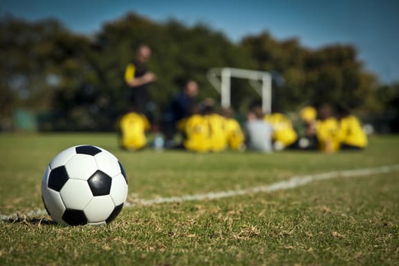 A soccer ball in the foreground, with a team of student players in the background.
