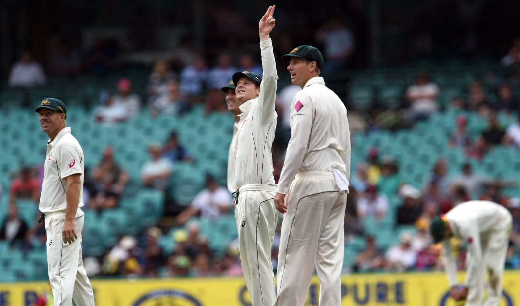 Australian captain Steve Smith (C) looks at the weather with team-mates Adam Voges (R) and David Warner (L) as rain delays the match against the West Indies on the second day of the third Test in Sydney on January 4, 2016. AFP PHOTO / William WEST