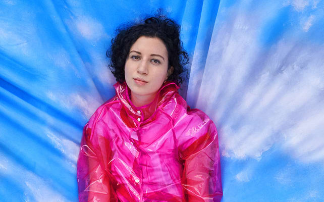 Young woman with dark curly hair wearing a bright pink jacket and black and white chequered pants