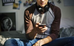 Teenage boy in a bedroom listening to music through his smartphone.