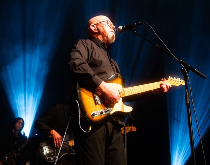 Dave Dobbyn faces the right with blue lights behind him.