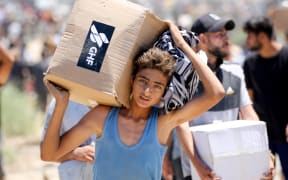 A boy carries a box of relief supplies from the Gaza Humanitarian Foundation (GHF), a private US-backed aid group that has bypassed the longstanding UN-led system in the territory, as displaced Palestinians return from an aid distribution centre in the central Gaza Strip on May 29, 2025. The humanitarian situation in Gaza, where aid has finally begun to trickle in after a two-month blockade, is dire following 18 months of devastating war between Israel and Palestinian Hamas movement. Food security experts say starvation is looming for one in five people. (Photo by Eyad BABA / AFP)