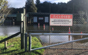A gate with a large 'closed until further notice' sign. Behind the gate, there is flooding form the nearby lake.