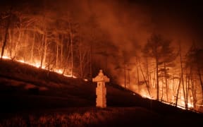 A wildfire is seen next to a stone lantern of family tomb in Andong on March 26, 2025. At least 18 people have been killed in one of South Korea's worst wildfire outbreaks, with multiple blazes burning and causing "unprecedented damage", the acting president said. (Photo by YASUYOSHI CHIBA / AFP)