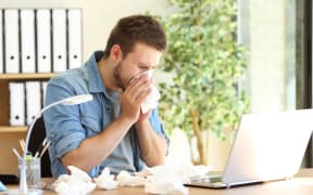 Portrait of a sick entrepreneur blowing in a wipe at office with a lot of used wipes on the desk
