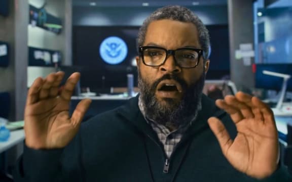 Ice Cube, a Black man with a beard and glasses, raises his hands and opens his mouth in surprise.