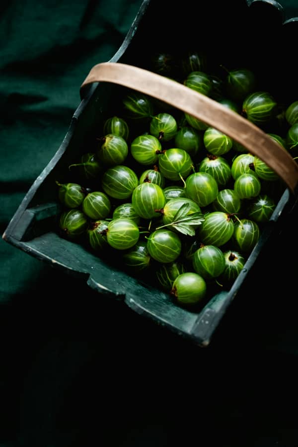 A wooden tray of green gooseberries