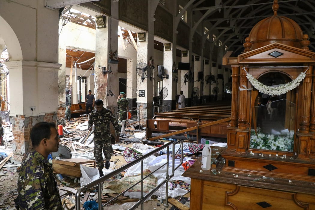 Sri Lankan security personnel walk past dead bodies covered with blankets amid blast debris at St. Anthony's Shrine following an explosion in the church in Kochchikade in Colombo on April 21, 2019.