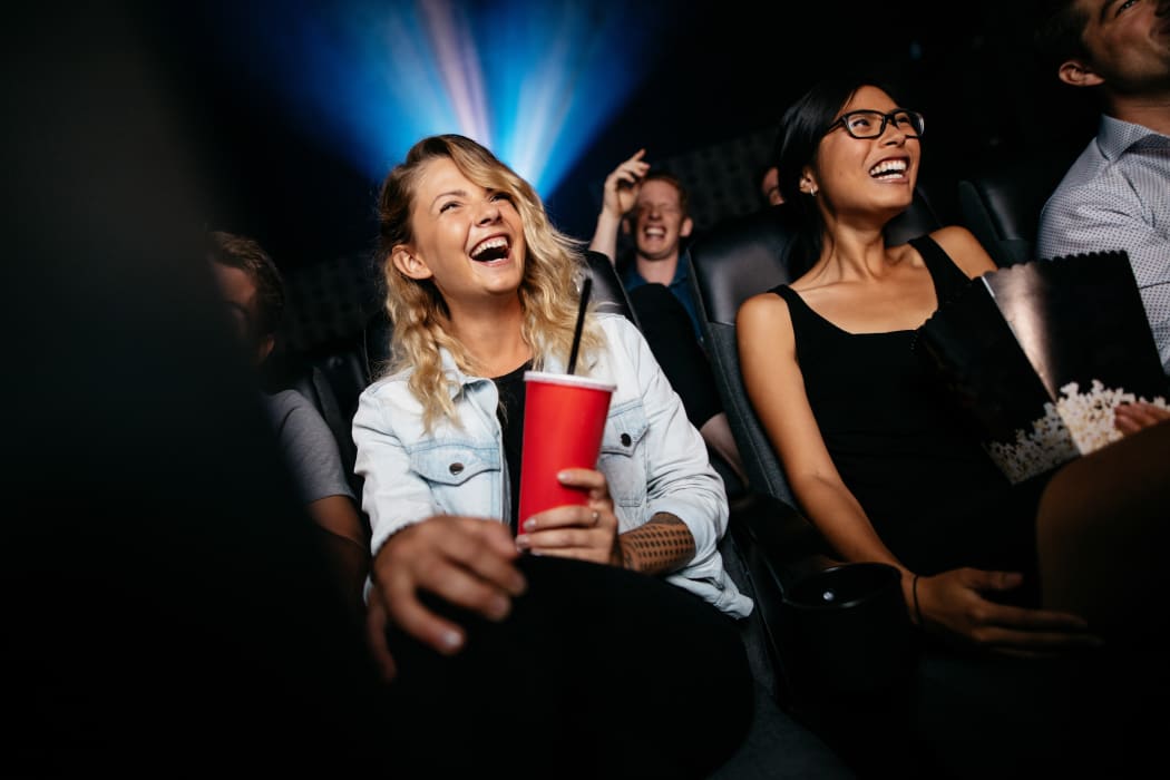 Young people laughing while watching film in movie theater.