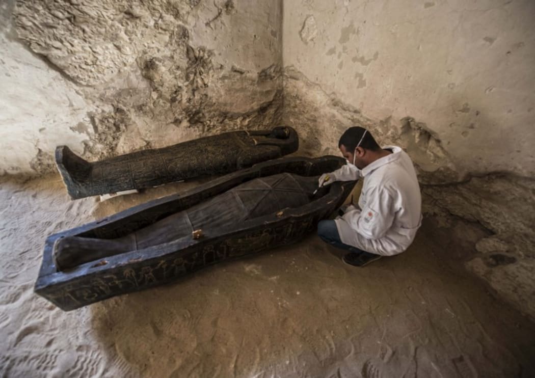 Egyptian archaeologist brushes a mummy laid inside a carved black wooden sarcophagus inlaid with gilded sheets. Discovered between the royal tombs at the Valley of the Queens and the Valley of the Kings.