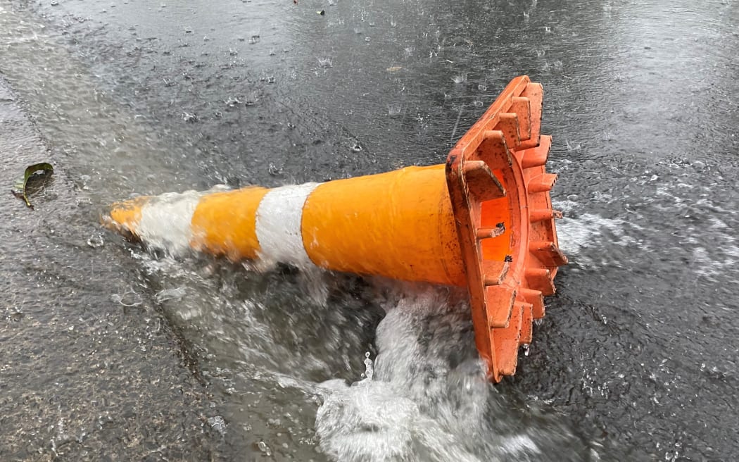 A road cone washed down a road in heavy rain.