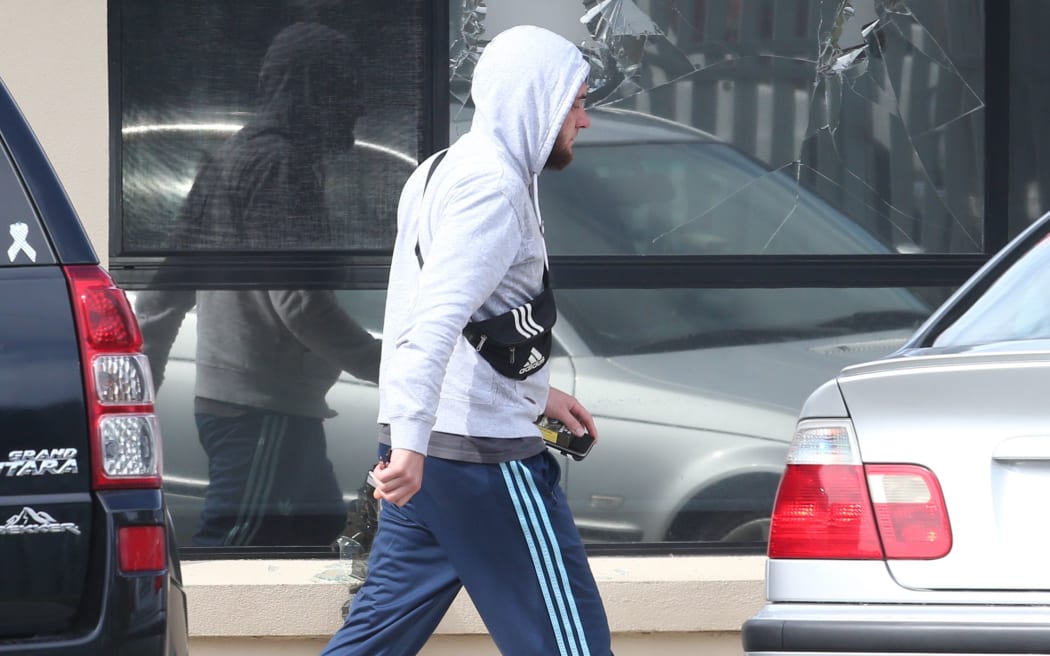 A man walks past a broken window from a police terror raid at a house in Melbourne, where police made one of several arrests.