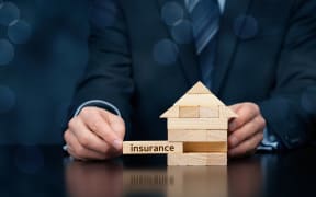 Property (family house) insurance protection concept. Insurance agent complete wooden model of the house with last piece with text insurance. Wide banner composition with bokeh background.