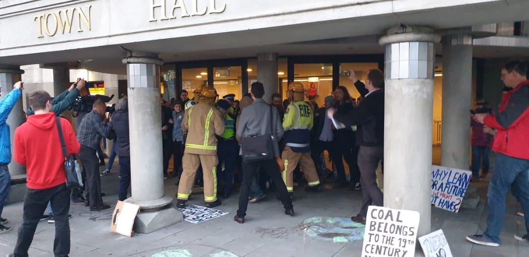 Firefighters and police officers have pushed through protesters with bolt cutters to try and cut chains placed on doors at the Dunedin Town Hall as people from the Stop the Minerals Forum Coalition chant outside.