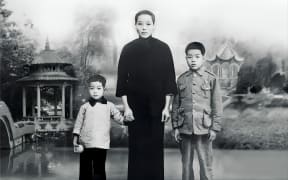 Lack and white photo of Chinese woman in traditional dress holding the hands of two children.