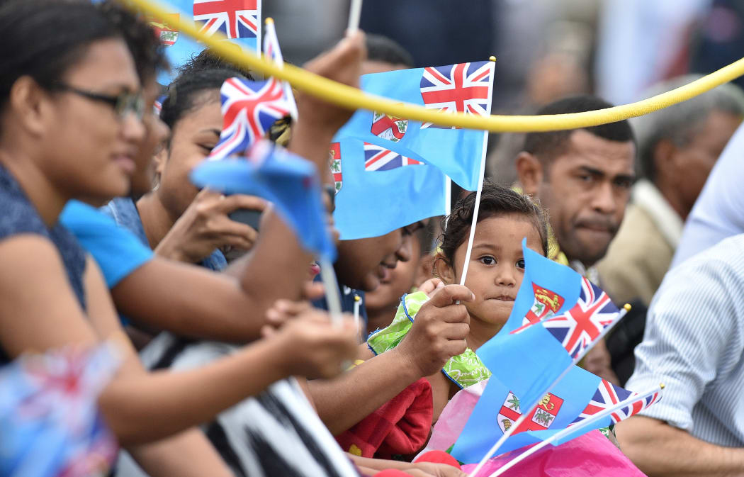 People wave British and Fijian flags as they wait for Britain's Prince Harry and his wife Meghan, the Duchess of Sussex, to arrive for a traditional welcome ceremony.