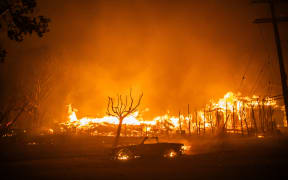 LOS ANGELES, CALIFORNIA - JANUARY 8: Flames from the Palisades Fire burns a car and homes during a powerful windstorm on January 8, 2025 in the Pacific Palisades neighborhood of Los Angeles, California. The fast-moving wildfire is threatening homes in the coastal neighborhood amid intense Santa Ana Winds and dry conditions in Southern California.   Apu Gomes/Getty Images/AFP (Photo by Apu Gomes / GETTY IMAGES NORTH AMERICA / Getty Images via AFP)