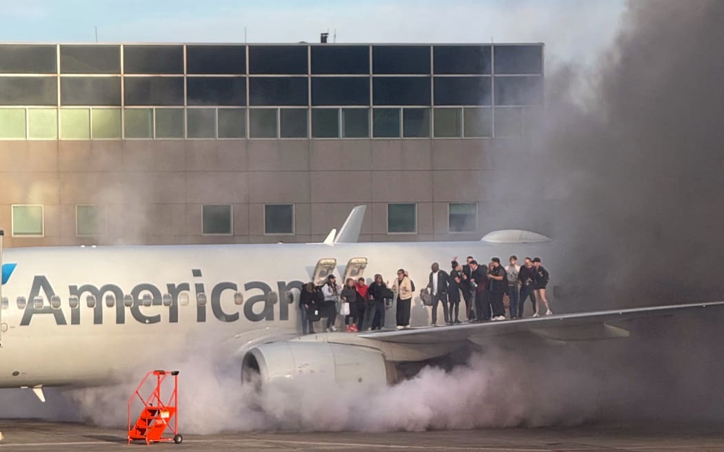 This image shows passengers standing on the wing of an American Airlines plane as they are evacuated after it caught fire while at a gate at Denver International Airport in Denver, Colorado, March 13, 2025.