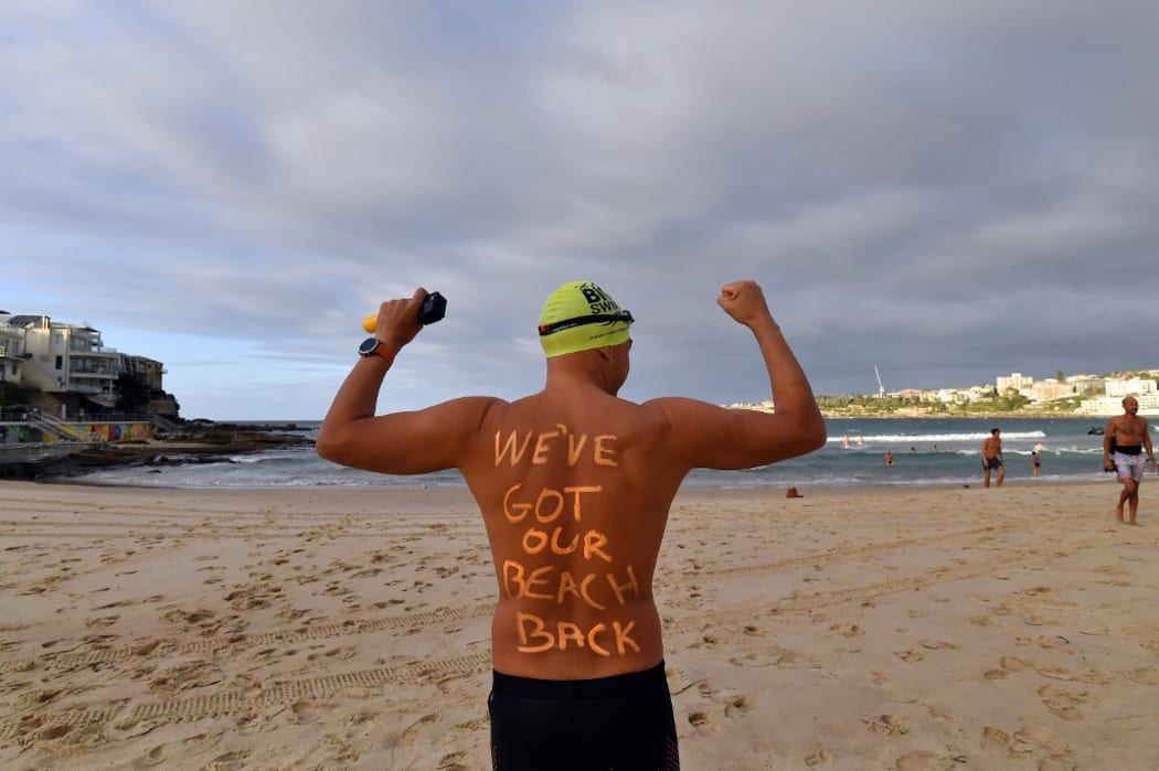 A man poses with a message on his back before enjoying his first swim after Bondi Beach reopened following a five week closure in Sydney on April 28, 2020.